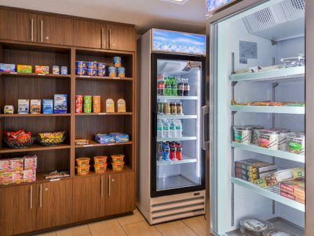 A small pantry with shelves of snacks, drinks, and instant noodles, next to refrigerated displays of beverages and ready-to-eat meals.