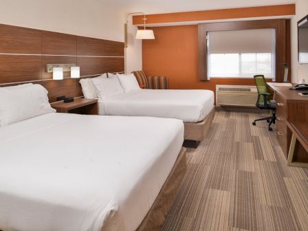 This image shows a hotel room with two beds, a desk, a chair, a flat-screen TV, modern decor, and a window.