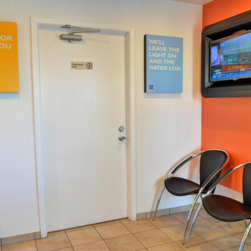 The image shows a small lobby area with two chairs, a TV on the wall, and two signs with promotional messages.