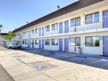 The image shows a two-story motel with blue doors, a parking lot, and designated accessible parking spaces in front.