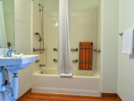 A bathroom with a sink, shower, and tub; featuring a curtain, towel, and handrails for accessibility, with a wooden floor.