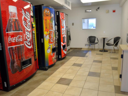 A room with vending machines, a small table, chairs, and a microwave on a counter.