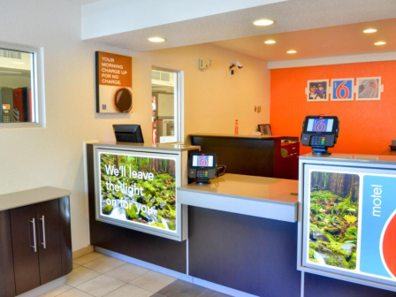 This image shows a Motel 6 reception area with two check-in counters, each with a computer terminal, and a welcoming interior design.