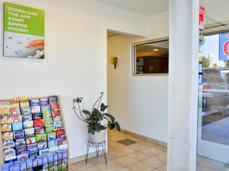 A small lobby area with a brochure rack, a wall poster for an app, a potted plant, and a glass door showing reflections outside.